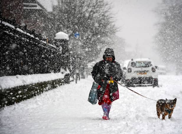 <p>A woman walks a dog through the snow in Glasgow on February 9, 2021</p>