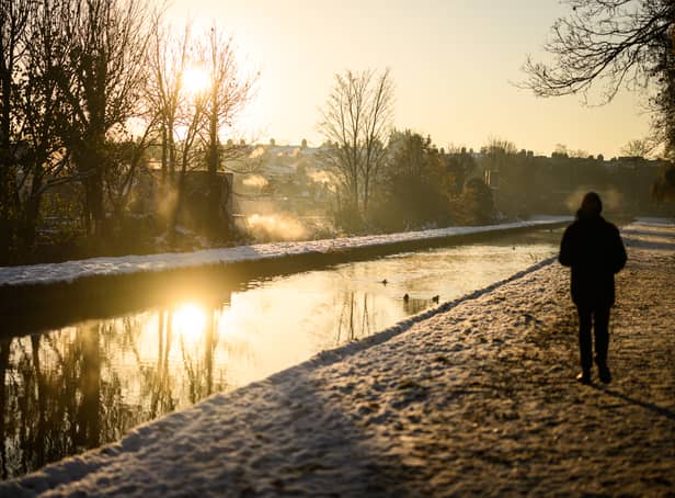 <p>A man walks on the snow-covered path by the New River at sunrise, as steam rises from nearby houses in London.</p>