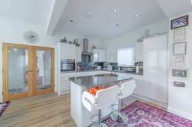 The kitchen has an island unit and is fitted with a range of modern white gloss base and wall units with the oven, hob and hood, fridge/freezer, dishwasher and washing machine to remain.