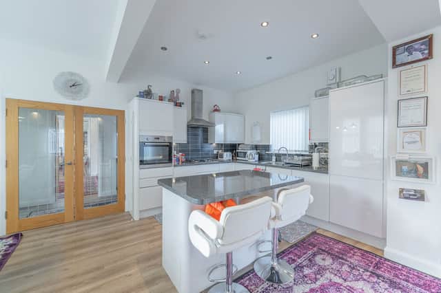 The kitchen has an island unit and is fitted with a range of modern white gloss base and wall units with the oven, hob and hood, fridge/freezer, dishwasher and washing machine to remain.