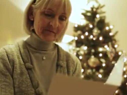 The woman sits at home reading her Christmas cards before being surprised by family.