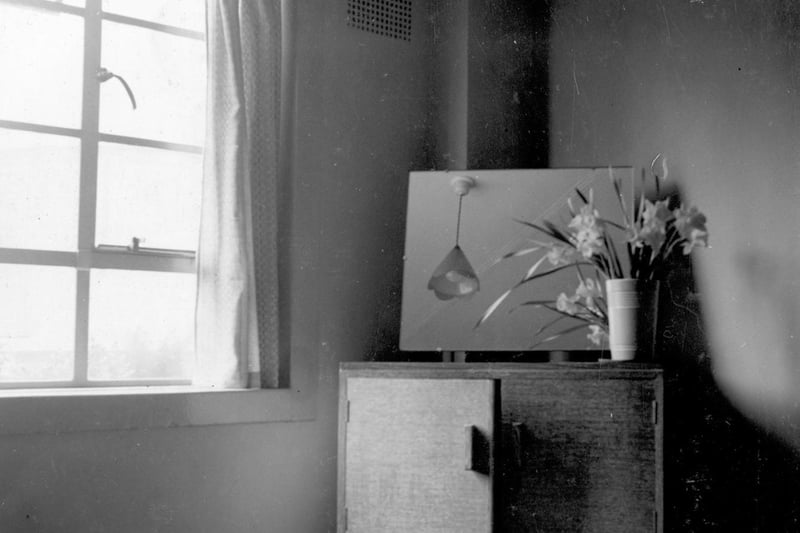 March 1938. The corner of a bedroom. A dressing table has a mirror and vase of daffodils.