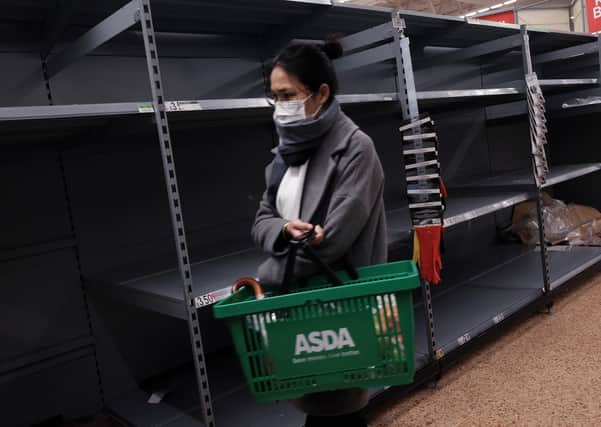 A shopper wearing a face mask walks past shelves emptied of toilet rolls – perhaps she’ll have to use newspapers instead (Picture: Yui Mok/PA Wire)