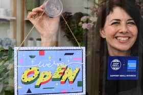 Michelle MacArthur from Moss Flowers in Glasgow displays a "WE'RE OPEN" sign designed by artist Yukai Du