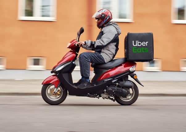 Uber Eats file photo of a delivery man riding his motor scooter on a street. Uber Brand Photography.