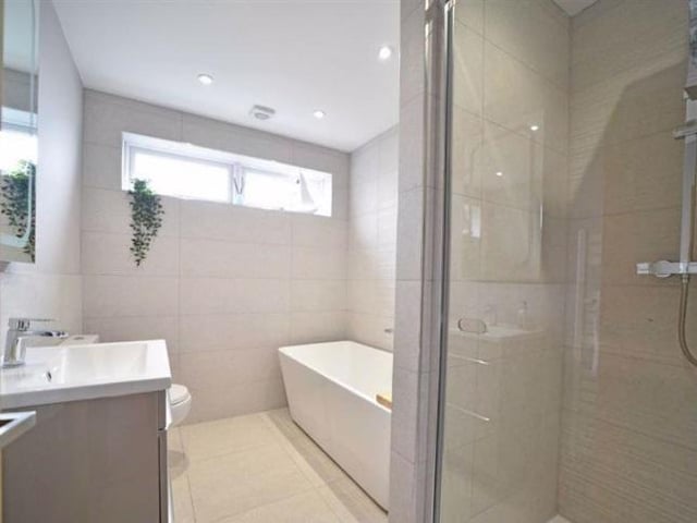 The family bathroom has a twin ended bath with a wall mounted mixer tap, vanity washbasin and ceramic tiled shower with a glazed pivot door, a heated towel rail and mounted mirror with lighting.