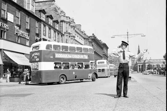 Policeman Ian Milne directs traffic in his shirt sleeves in Princes Street outside Marcus the Furrier during an Edinburgh heatwave in July 1962.