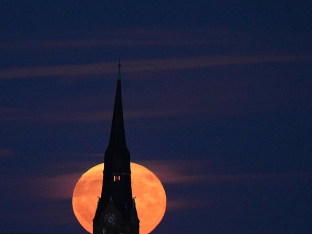The strawberry full moon rises behind a church in Berlin, Germany, Tuesday, June 14, 2022. (AP Photo/Markus Schreiber)