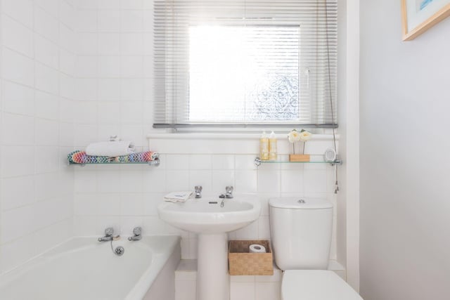 The property's bathroom  features a white three piece suite, electric shower over the bath and white full height tiling.