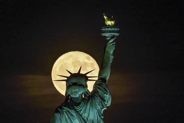 The Strawberry Supermoon rises in front of the Statue of Liberty in New York, late Tuesday, June 14, 2022. (AP Photo/J. David Ake)