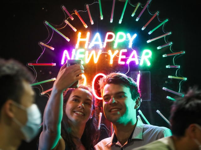 People seen having their photo taken in front of a neon Happy New Year sign as people wearing masks walk past during New Year's Eve celebrations on December 31, 2020 in Melbourne, Australia. Celebrations look different this year as COVID-19 restrictions remain in place due to the ongoing coronavirus pandemic.