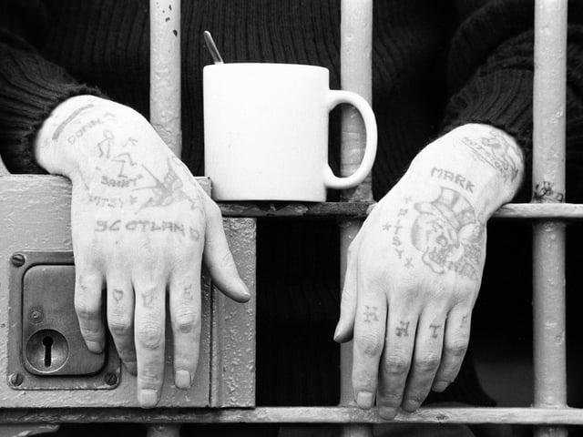 Prisoner Ronnie Farmer's hands are visible through the bars of his cell, with a mug of tea sitting on a bar. The photo was taken at Saughton Prison in June, 1994.