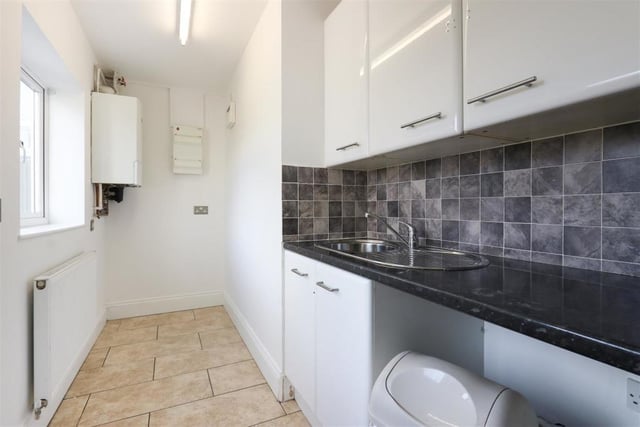 White wall and base units, tiled splashback and flooring are features of the utility room which houses the central heating boiler.