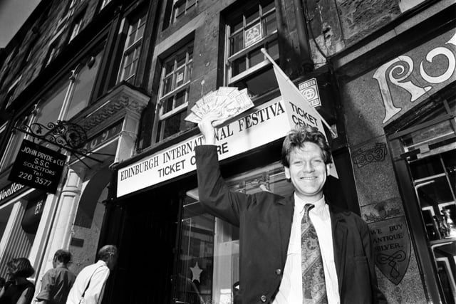 British actor Kenneth Branagh holds up some leaflets outside the Edinburgh Festival's new box office by St Giles Cathedral in the Royal Mile, August 1990.