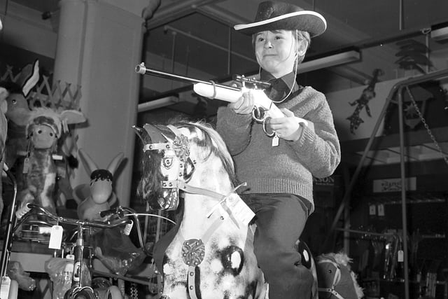 Little boy with a cowboy hat and a toy rifle on a rocking horse - the toy department of Jenners' store, Edinburgh in December 1977.
