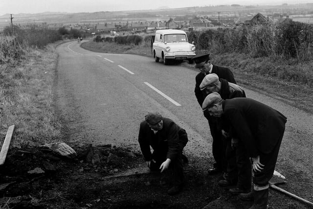 Workmen examine a deep crater in a road near Tranent in November 1964.