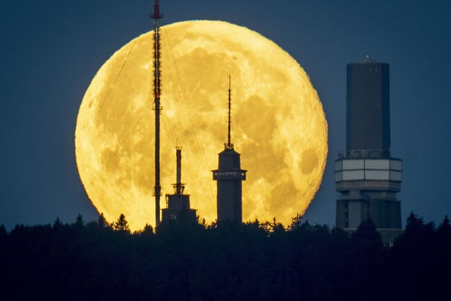 The full moon sets behind the telecommunication devices on top of the Feldberg mountain near Frankfurt, Germany, early Wednesday, June 15, 2022.In Frankfurt, it rose behind the German city’s banking district’s skyline.  (AP Photo/Michael Probst)