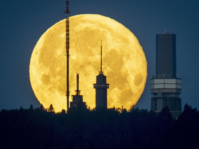 The full moon sets behind the telecommunication devices on top of the Feldberg mountain near Frankfurt, Germany, early Wednesday, June 15, 2022.In Frankfurt, it rose behind the German city’s banking district’s skyline. (AP Photo/Michael Probst)