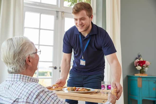 Stock photo of a male care worker serving dinner to a senior man at his home.