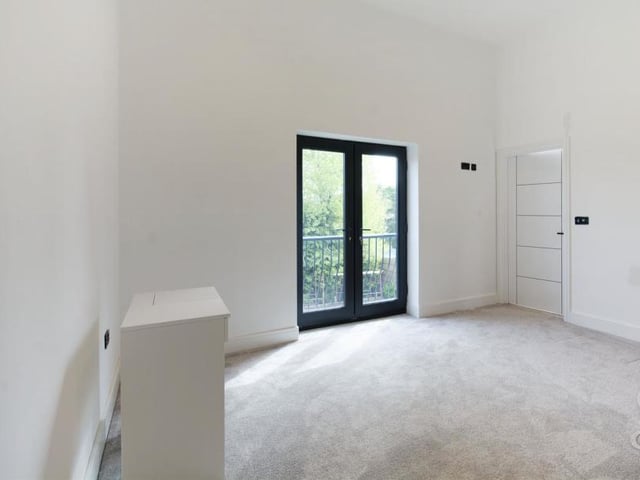 A Juliet balcony is a key feature of one of the bedrooms. The room also has a carpeted floor and a central-heating radiator.