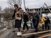 A woman carries her dog as she flees the fighting in the Ukrainian city of Irpin via a destroyed bridge (Picture: Chris McGrath/Getty Images)
