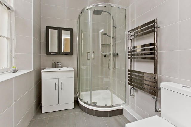 The contemporary en-suite shower room comprises a cubicle with a rainfall showerhead, a WC-suite, vanity storage, and a towel radiator.