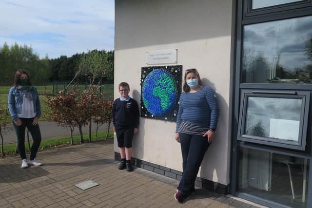 Harris Diamond (P4) is pictured in the centre with Elinor Fox on the left. Harris’s world design became a stunning mosaic thanks to Maria Campbell, on far right, who used recycled bottle tops.