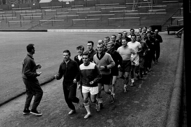 A group of referees join Hearts players for their pre-season training, with the Tynecastle terracing in the background, in August 1965.