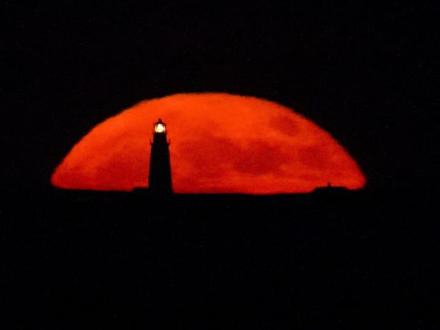 A full moon rises behind the Boston Light, in Winthrop, Mass. Picture (AP Photo/Julio Cortez)
