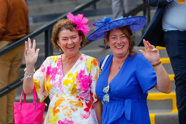 Two well-dressed guests wave to the camera as they wait for the first race to begin.
