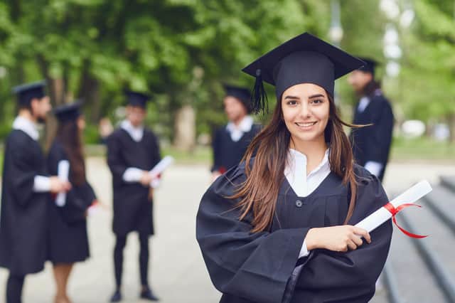 A young female graduate with a scroll in her hands is smiling against the background of university graduates. Graduation.University gesture and people concept.