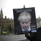 A protester holds a placard with an image of British Prime Minister Boris Johnson including the words "Now Partygate" backdropped by the Houses of Parliament