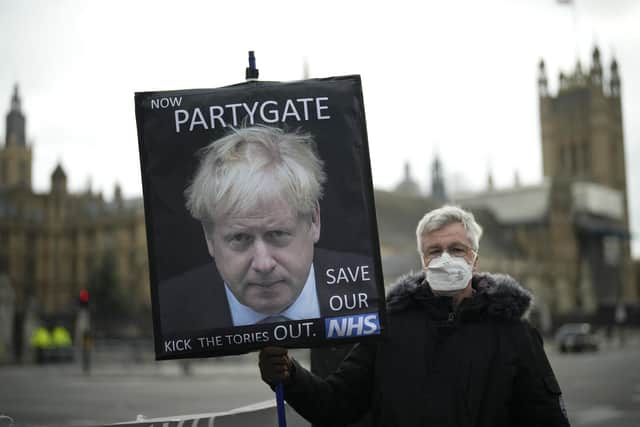 A protester holds a placard with an image of British Prime Minister Boris Johnson including the words "Now Partygate" backdropped by the Houses of Parliament