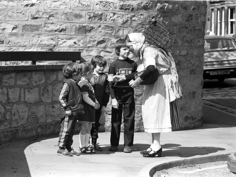 With her basket on her back, traditionally-dressed fishwife Nan Oliver takes her seafood and shellfish round the Trinity area of Edinburgh in May 1982. These children seem unsure of the cockles she offers them.