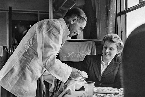A female passenger is served by a waiter in the dining car of the Flying Scotsman express passenger train service operating between the capital cities of Edinburgh and London by the London and North Eastern Railway (LNER), 8th October 1945.