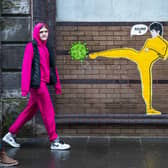 Members of the public walk past a piece of street art by 'Palley' that features Bruce Lee kicking a coronavirus molecule in Glasgow's East End.