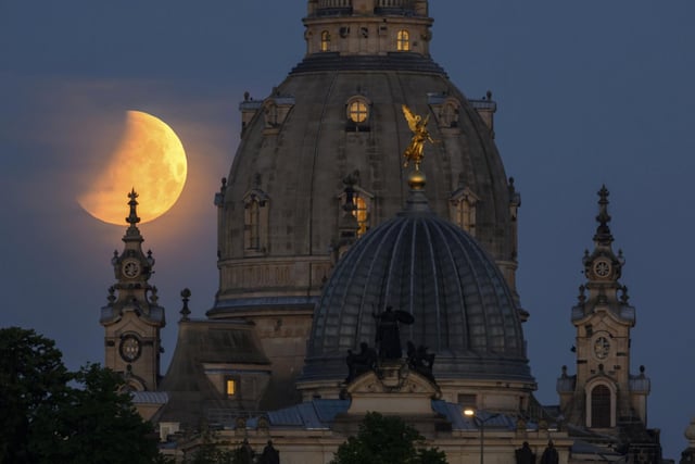 The moon sets in the morning during a partial lunar eclipse behind the Frauenkirche and the dome of the Kunstakedmie with the angel "Fama" in Dresden, Germany (Robert Michael/dpa via AP)