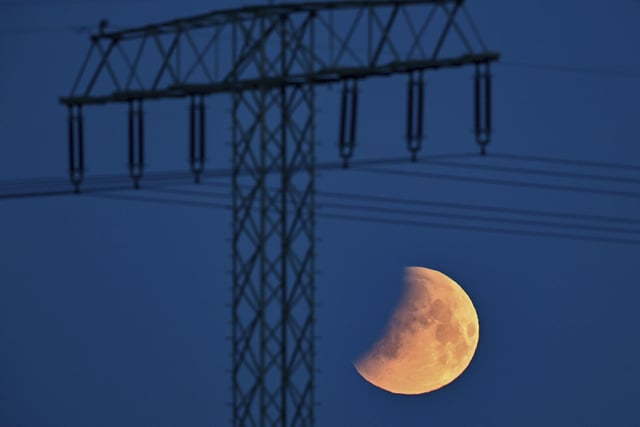 The beginning of the lunar eclipse is seen in the early morning next to a high voltage pylon in Jacobsdorf, Germany (Patrick Pleul/dpa via AP)