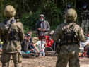 A group of migrants believed to be from Afghanistan sit between between Polish (foreground) and Belarusian (background) security forces near the Poland-Belarus border (Picture: Wojtek Radwanski/AFP via Getty Images)
