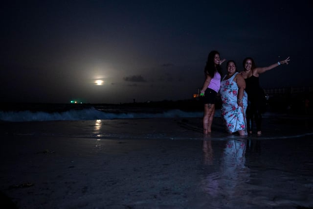 People pose for a picture as they gather to watch a full moon, the "Strawberry supermoon", as it rises in Miami Beach, Florida on June 14, 2022 (Photo by CHANDAN KHANNA/AFP via Getty Images)