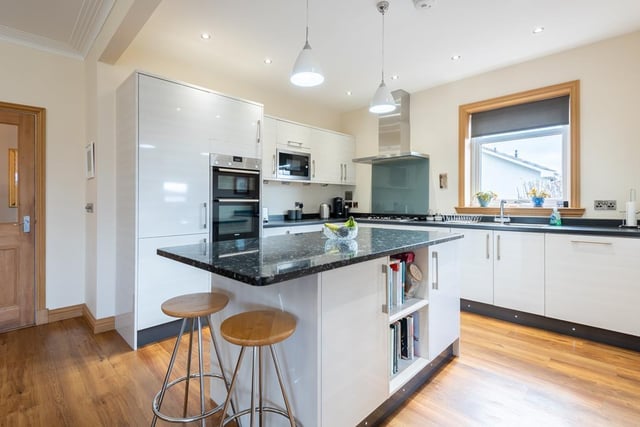 The contemporary fitted kitchen has wall mounted, floor standing units with contrasting granite work top, breakfast island, and integrated appliances.