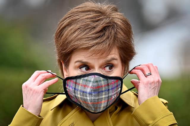 Nicola Sturgeon puts on a Covid face mask (Picture: Jeff J Mitchell/PA)