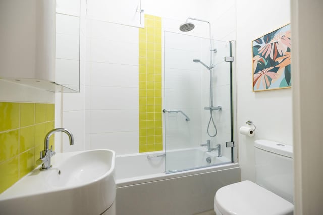 The partially-tiled bathroom has a three-piece white suite with a WC, curved basin and a wall-mounted rainfall shower over the bath.
