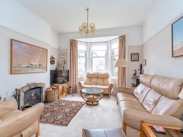 The south-facing bay-windowed living room overlooking the private front garden. It features an appealing neutral décor, built-in shelving, and focal open Jetmaster fire with exposed brickwork hearth and surround.
