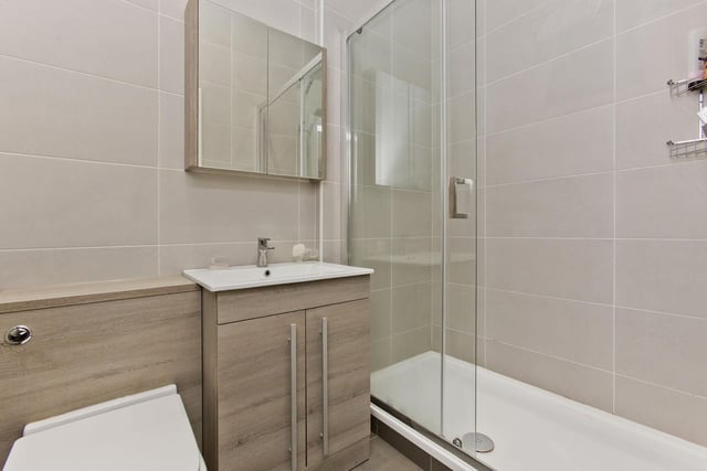 The separate family shower room comes complete with an oversized enclosure with a rainfall shower, a WC-suite set into storage, and a wall-mounted, mirrored vanity unit.