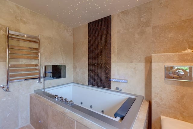 The family bathroom comprises his and hers polished stone wash hand basins, an inset spa bath and recessed television, and a separate shower enclosure with a fitted rain head shower.
