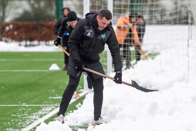 Jack Ross helps clear snow off the training pitch prior to Hibs training at the HIbernian Training Centre