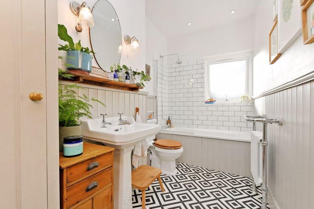 The bathroom has a white suite with a shower above the bath and a glass screen, plus a wash basin, WC, stylish tiling and panelling, a tiled effect cushioned floor and useful storage units.