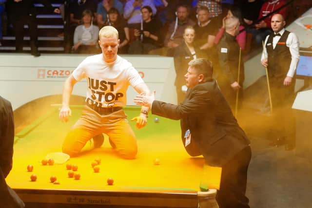 A Just Stop Oil protester is removed after jumping on the table and throwing orange powder during the match between Robert Milkins against Joe Perry during day three of the Cazoo World Snooker Championship at the Crucible Theatre, Sheffield.