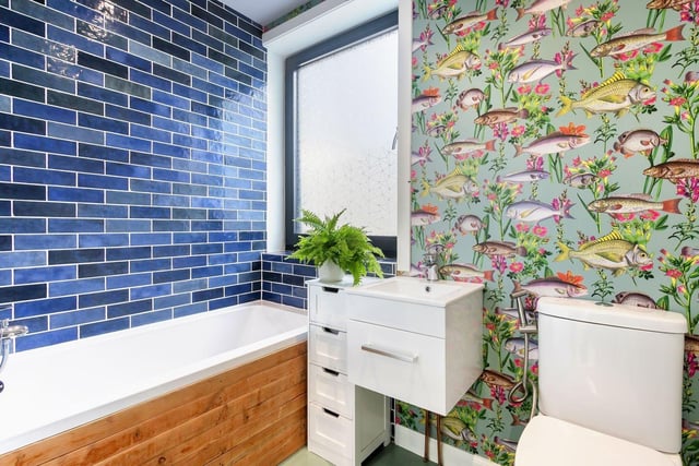 The three-piece family bathroom by the living area is finished with aqua-hued tiles and nautical-themed décor. This chic space is comprised of a toilet with a bidet hose, a storage-set washbasin, and a bath with a handheld shower.